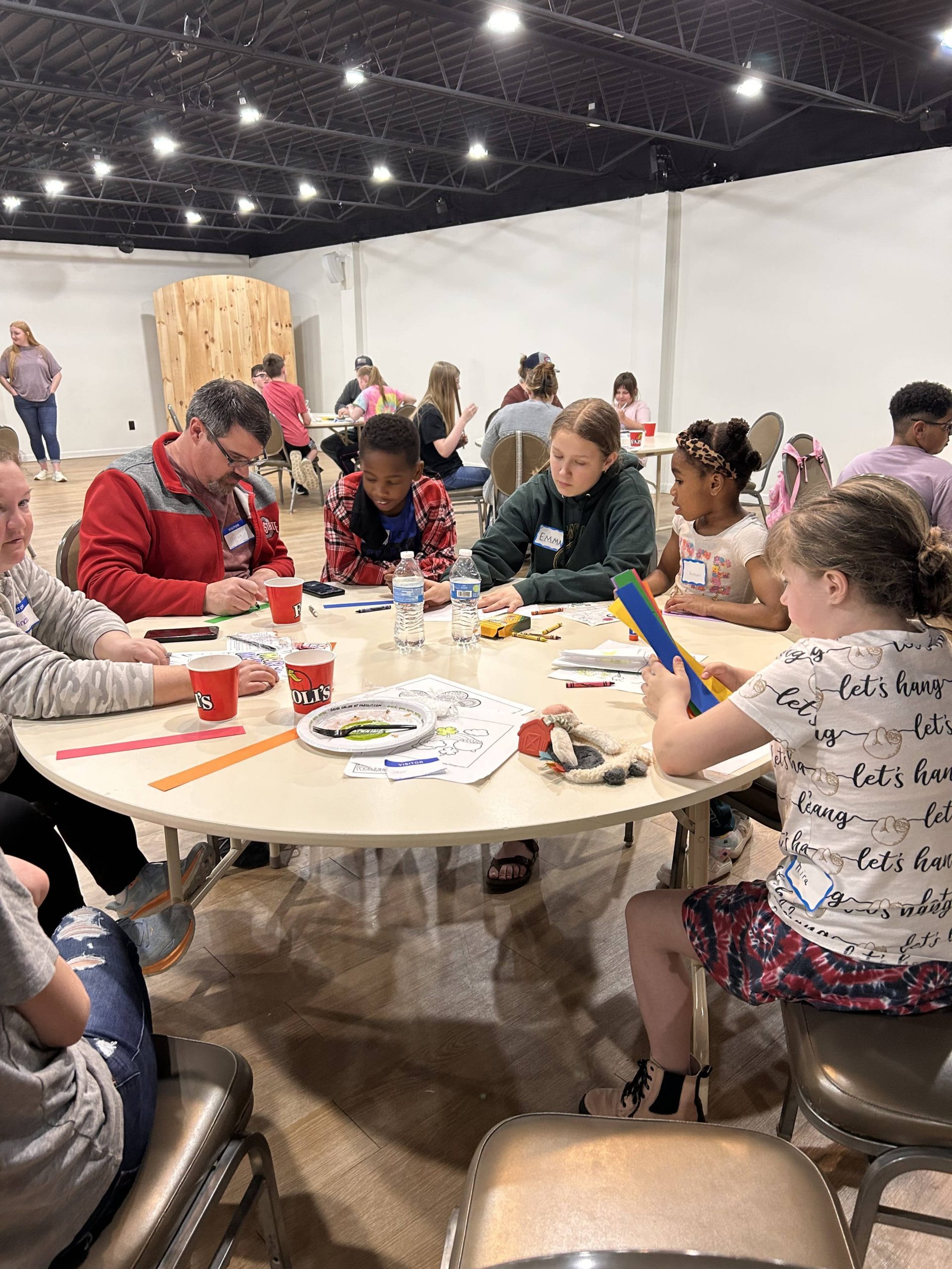 A group of 2 adults and 4 children sitting at a table doing a craft