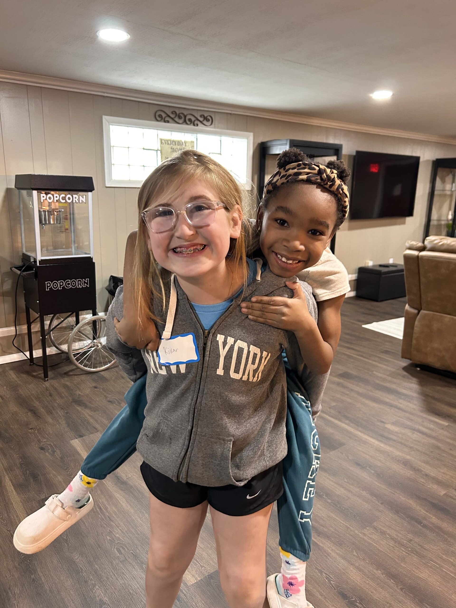 Two girls giving each other a piggy back ride and smiling at the camera