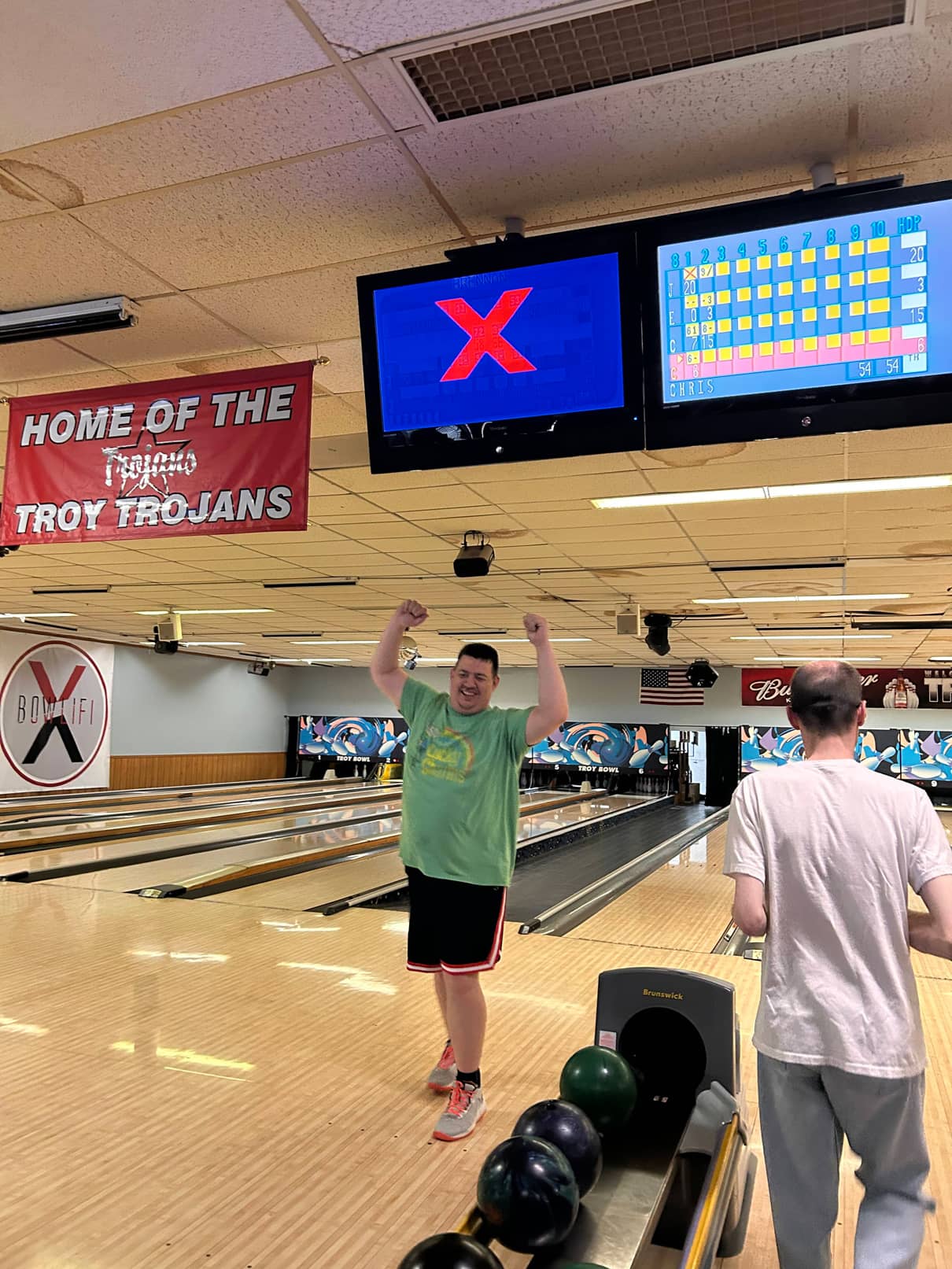 A man cheering in front of a bowling lane after bowling a strike