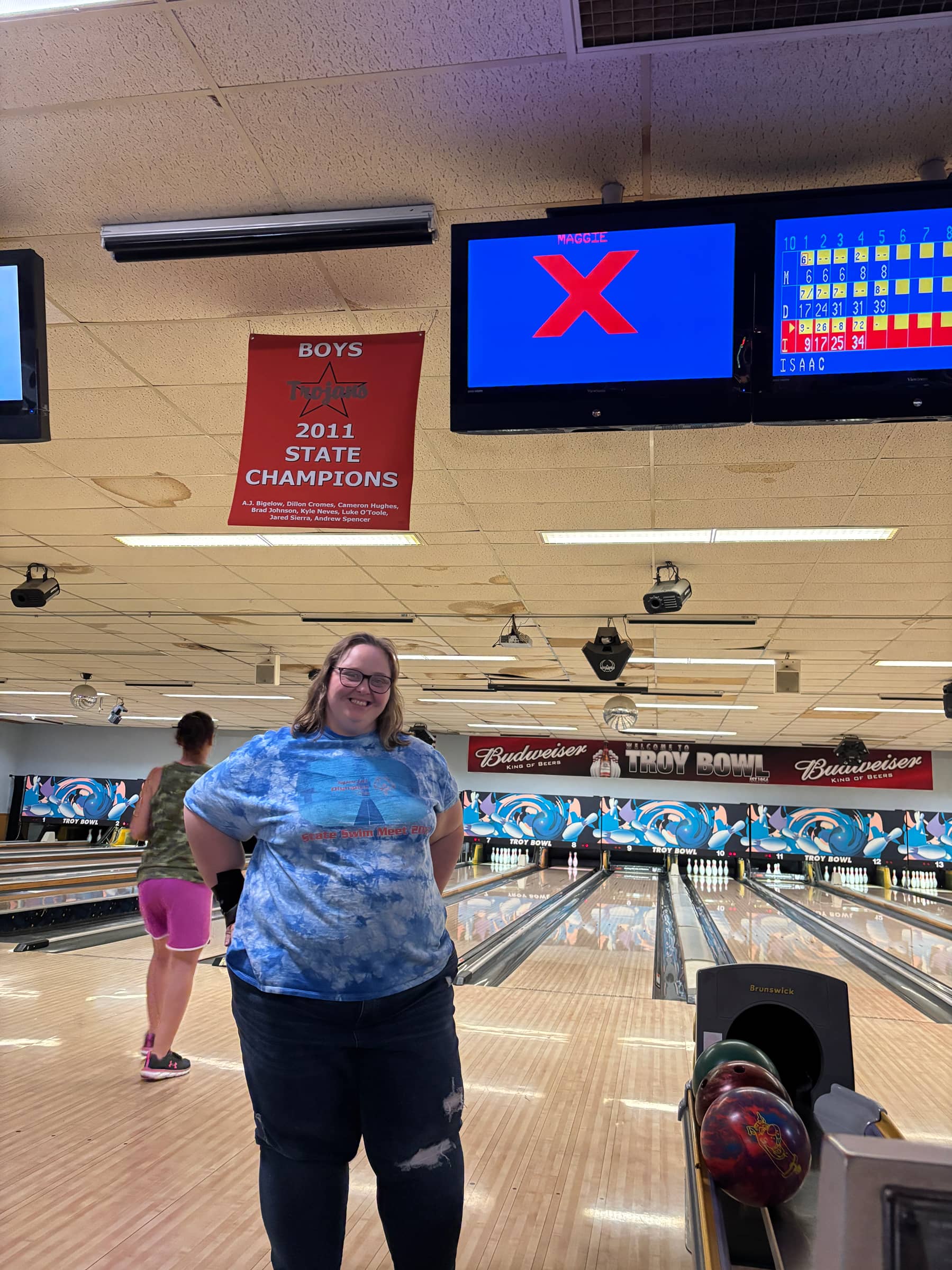 A woman standing in front of a bowling lane smiling after she bowled a strike 